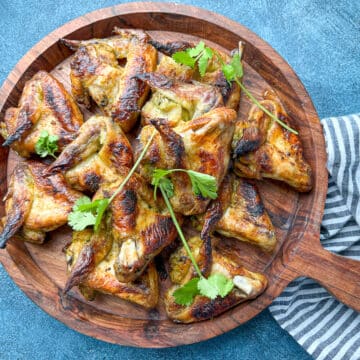 overhead shot of baked marinated whole chicken wings on wooden serving tray next to striped gray napkin.