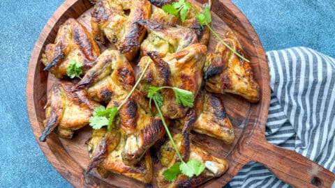 overhead shot of baked marinated whole chicken wings on wooden serving tray next to striped gray napkin.