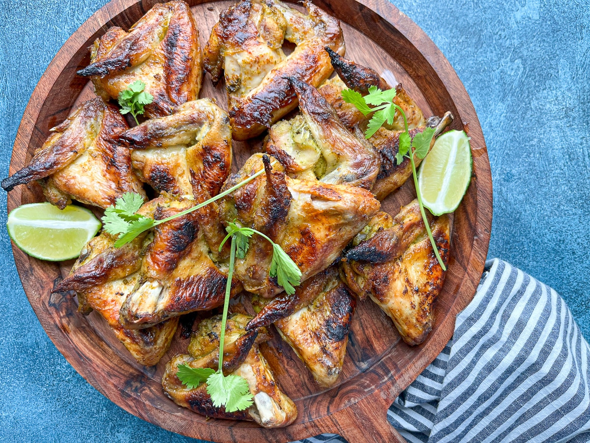baked marinated whole chicken wings on round wooden tray with lime wedges.