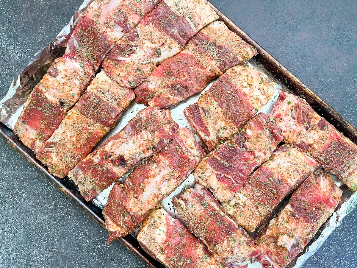 raw seasoned ribs arranged on baking sheet in single layer.