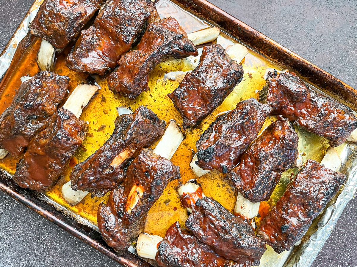 broiled beef back ribs with BBQ sauce on baking sheet.