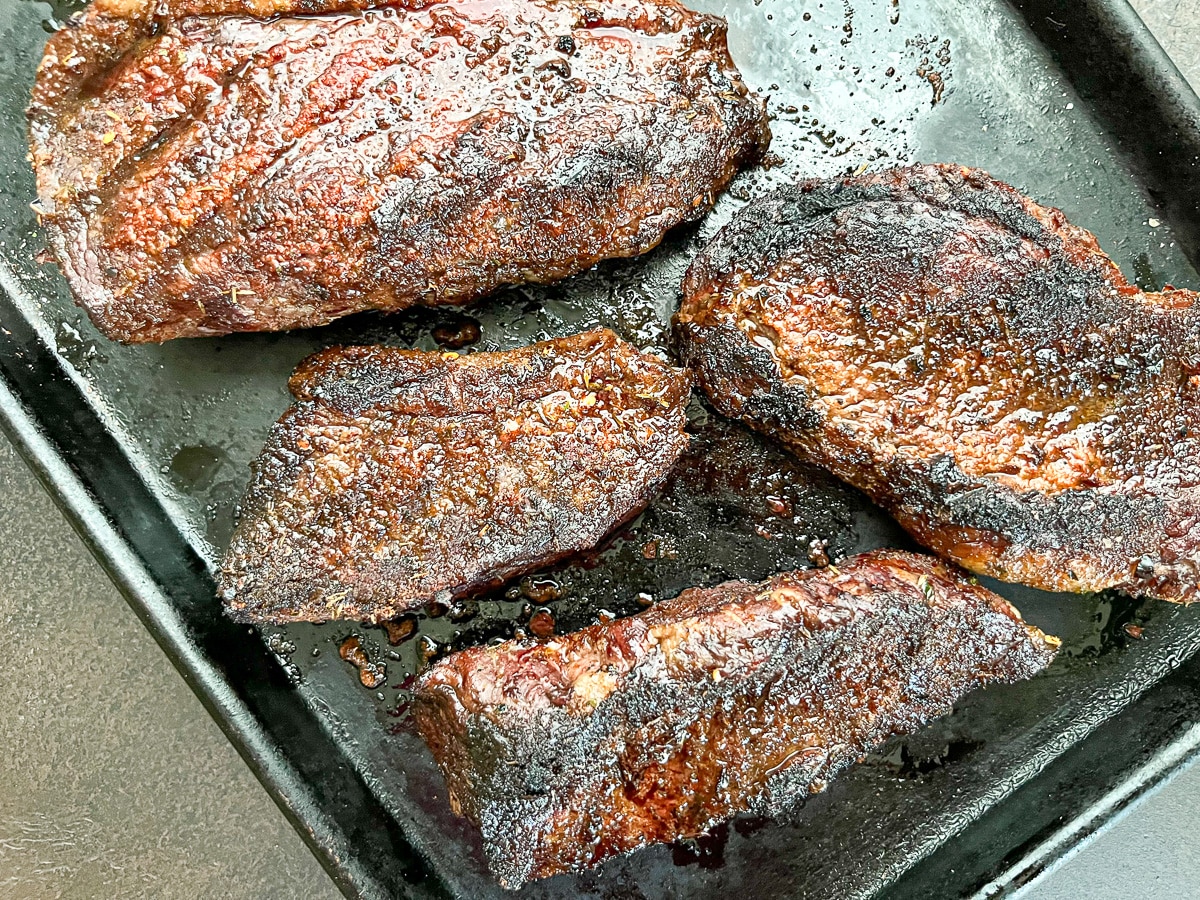close-up shot of grilled top sirloin cap steak on lined baking sheet.