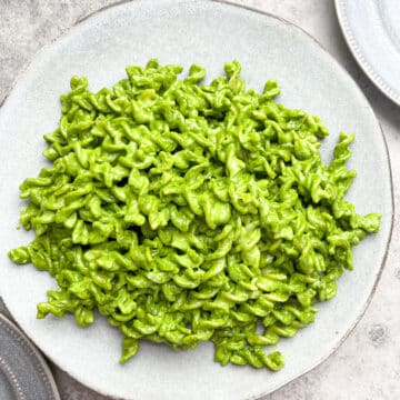 pesto pasta in large gray plate with smaller gray plates on either side of the larger plate.