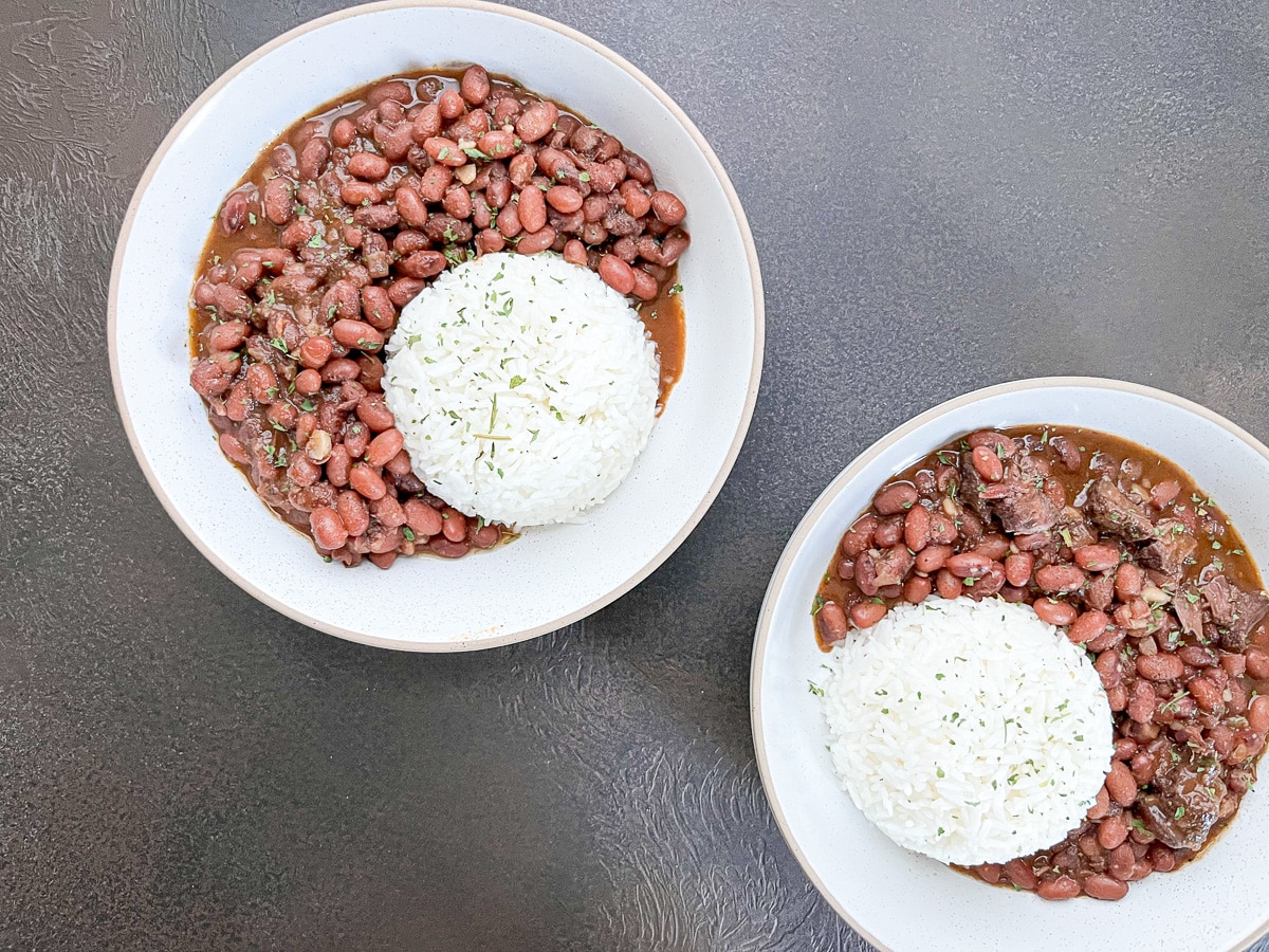 Two white bowls with Cajun red beans inside topped with a scoop of rice.