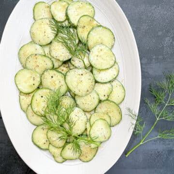 Italian cucumber salad in a white oval serving dish garnished with fresh dill with dill also on the side.