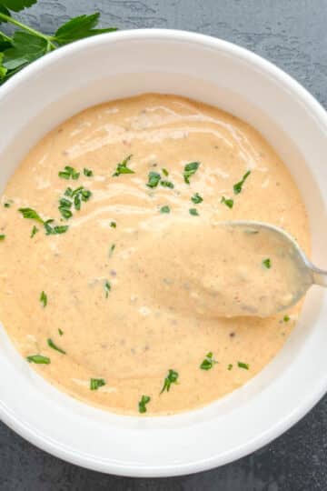 Cajun remoulade dipping sauce in a white bowl with a spoon with the sauce dripping from it.