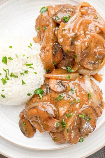 Smothered hamburger steaks and rice on white plate.