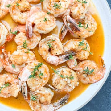 Louisiana BBQ Shrimp on a white plate garnished with fresh thyme.