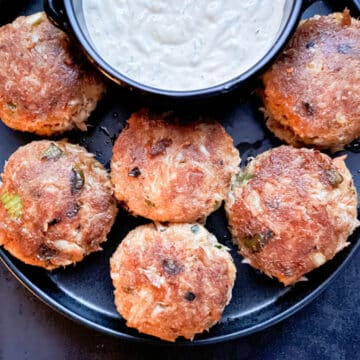 Overhead shot of golden brown crab cakes with crispy edges, plated with smoky jalapeño tartar sauce in a small dipping bowl. Crab cakes are arranged in front of dipping sauce.