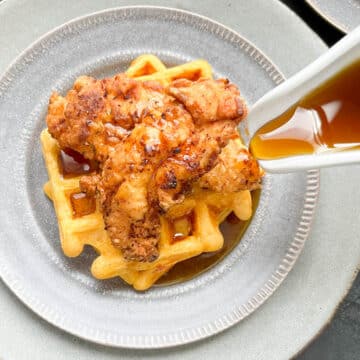 Waffles on a gray plate topped with fried chicken with a generous pour of maple syrup.