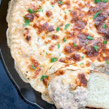 Creamy baked Cajun crab dip in a cast iron skillet, fresh from the oven, with a slice of French bread for dipping.