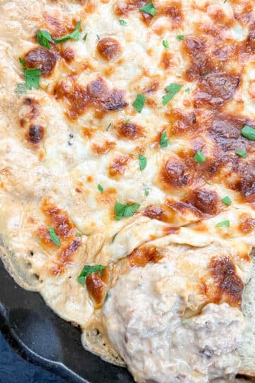 Creamy baked Cajun crab dip in a cast iron skillet, fresh from the oven, with a slice of French bread for dipping.