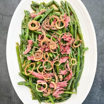 Overhead shot of green beans topped with crispy shallots and shredded smoked turkey neck, ready to be served.
