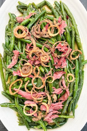 Overhead shot of green beans topped with crispy shallots and shredded smoked turkey neck, ready to be served.