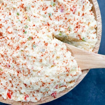 Southern-style potato salad, sprinkled with smoked paprika, served in a wooden bowl with a portion being lifted by a spoon.