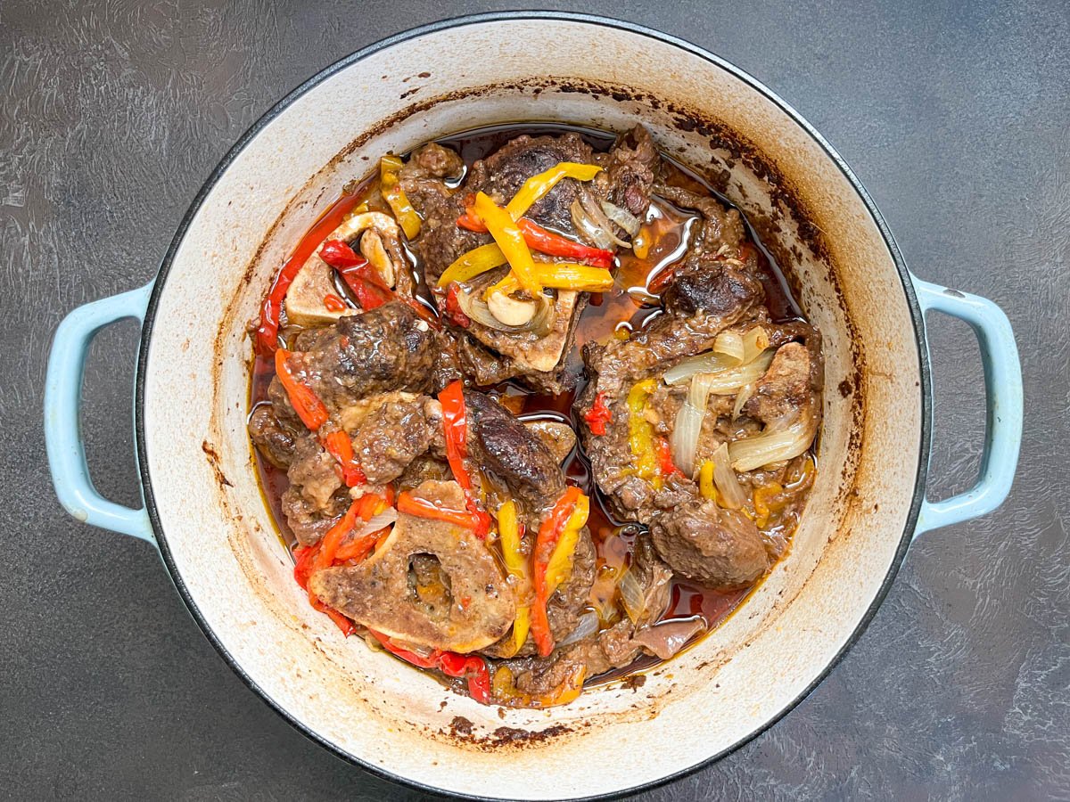 Braised beef shanks in Dutch oven after slow cooking, surrounded by onion, bell pepper, and garlic in a rich Southern-style sauce.
