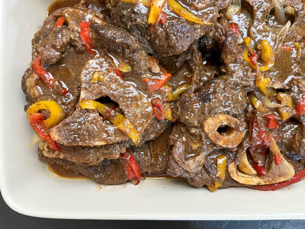 Close-up of braised beef shank topped with onion and bell peppers, showing fork-tender texture in a rich Southern-style sauce.