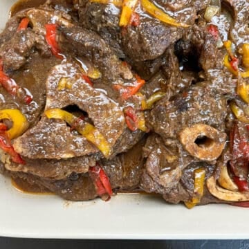 Close-up of braised beef shank topped with onion and bell peppers, showing fork-tender texture in a rich Southern-style sauce.