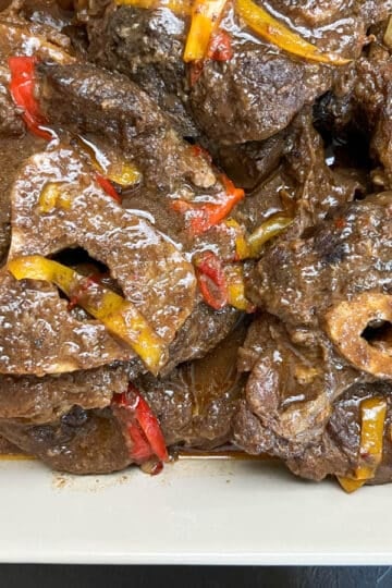 Close-up of braised beef shank topped with onion and bell peppers, showing fork-tender texture in a rich Southern-style sauce.