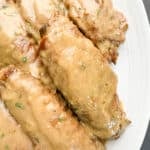 Close-up image of tender turkey wings smothered in homemade gravy on a white oval platter, ready to serve.
