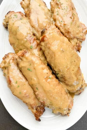 Overhead shot of smothered turkey wings served on a white oval platter with homemade onion garlic gravy.