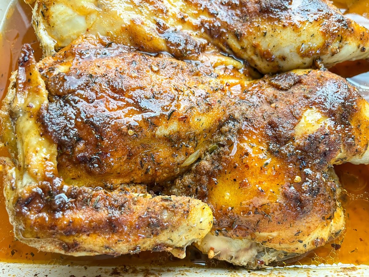Close-up of Southern baked spatchcock chicken with golden skin, drizzled with hot honey glaze and pan juices.
