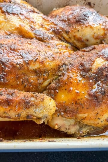 Southern baked spatchcock chicken in a white baking dish, drizzled with hot honey glaze and surrounded by pan juices.