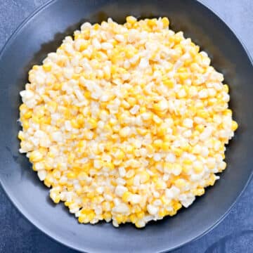 Southern fried corn with sauteed shallots and yellow bell pepper, served in a black bowl.