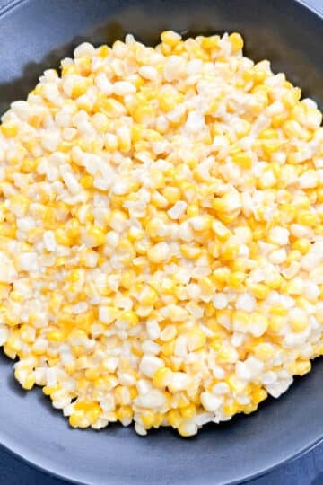 Southern fried corn with sauteed shallots and yellow bell pepper, served in a black bowl.