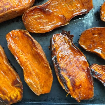 Caramelized roasted sweet potatoes on a parchment-lined baking sheet, fresh out of the oven.