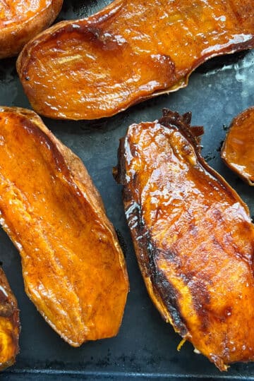 Caramelized roasted sweet potatoes on a parchment-lined baking sheet, fresh out of the oven.