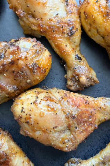 Close-up shot of baked chicken legs arranged on a black dinner plate.